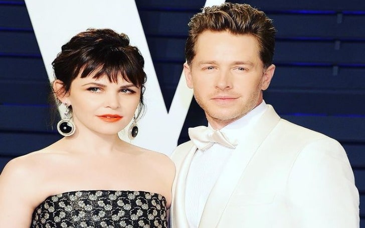 Josh Dallas in a white suit with his wife in a black and white designed dress and black earring.